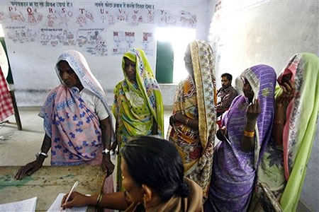 An election official, seated, checks the identity of women at a polling station, in Jamuva Bazar, near Varanasi, India, Thursday, April 16, 2009.